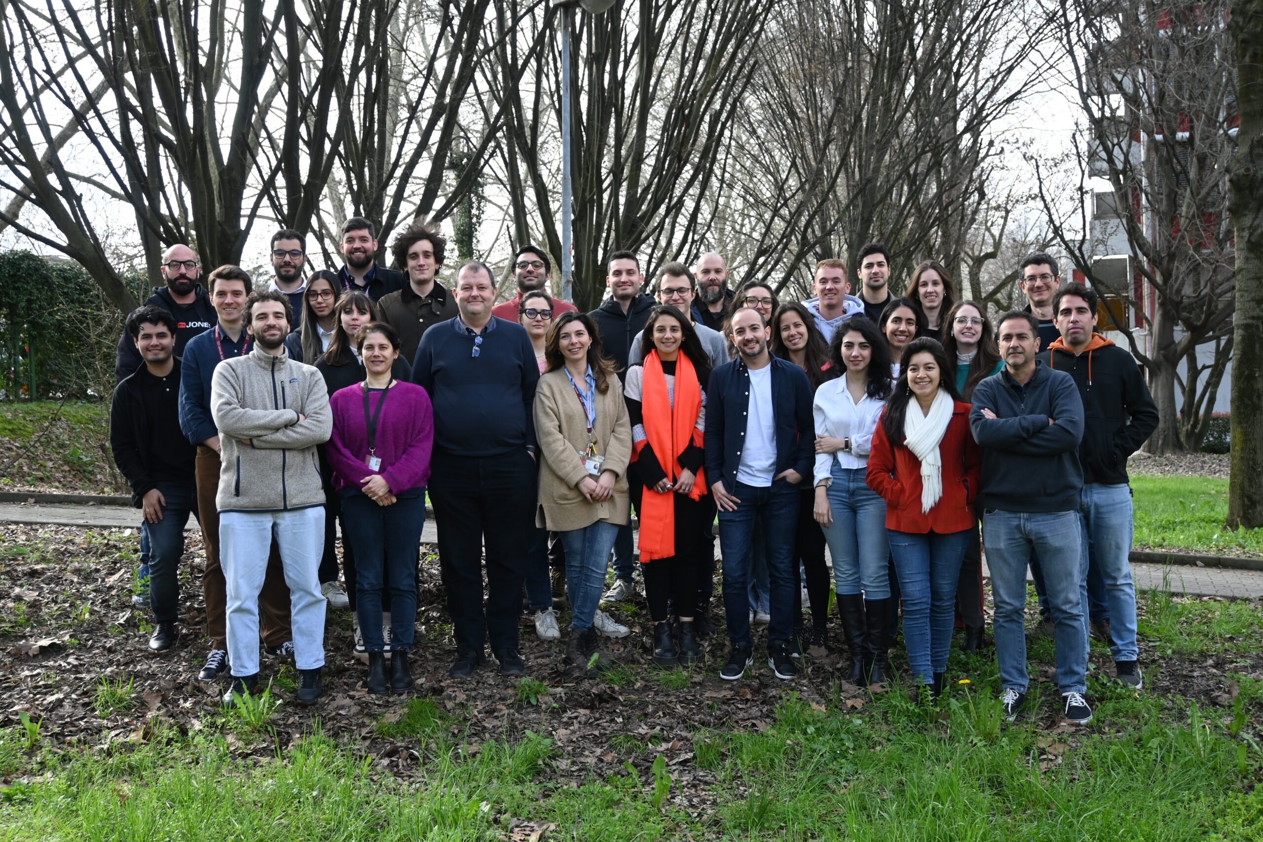 A diverse group of people standing together in a sunny park, surrounded by trees and green grass