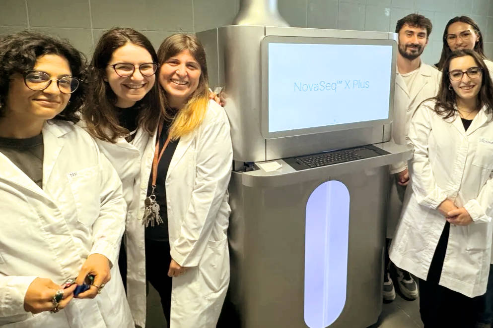 A group of people in lab coats stands beside a sequencer machine.