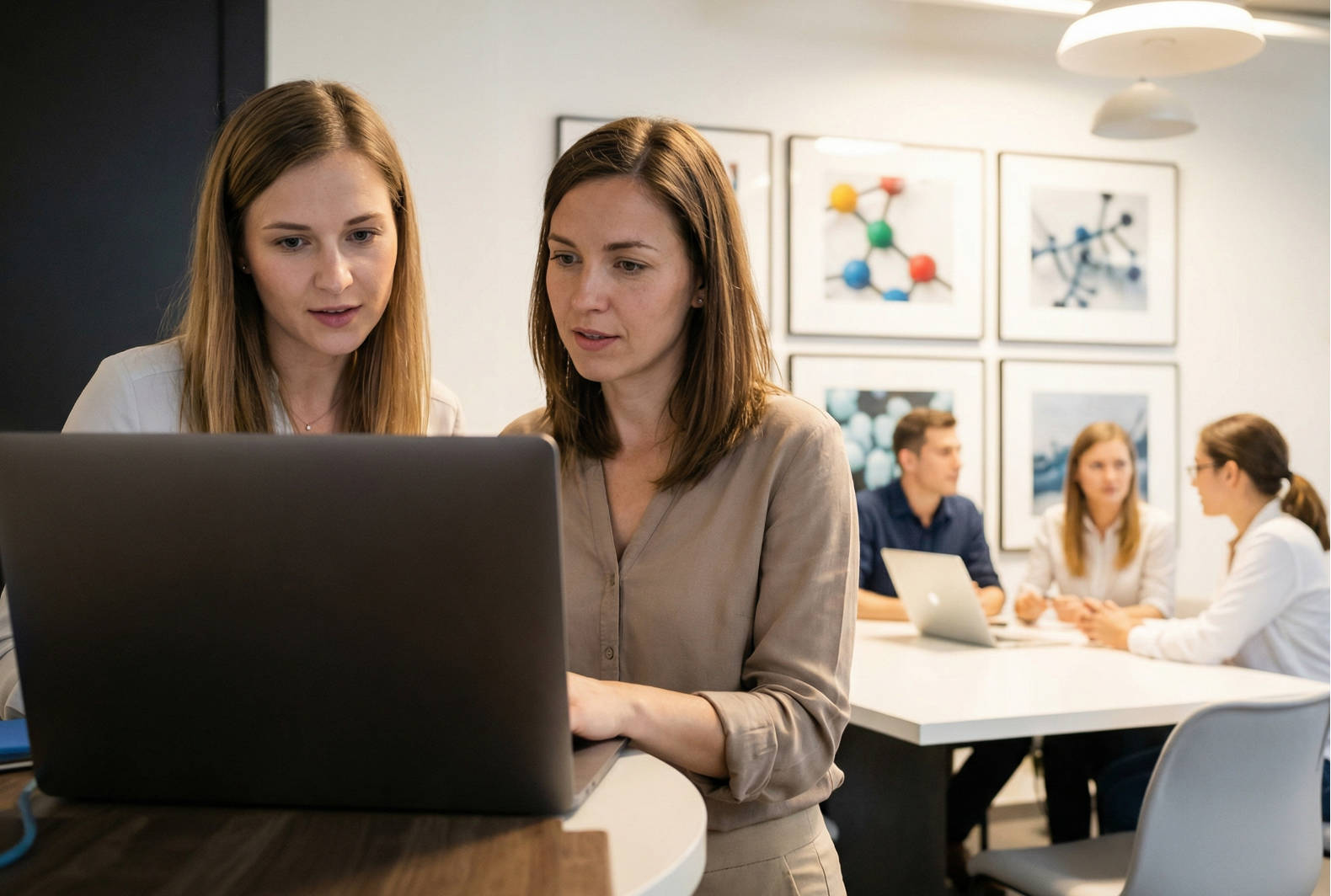 Two women in an office engaged in discussion while viewing a laptop together
