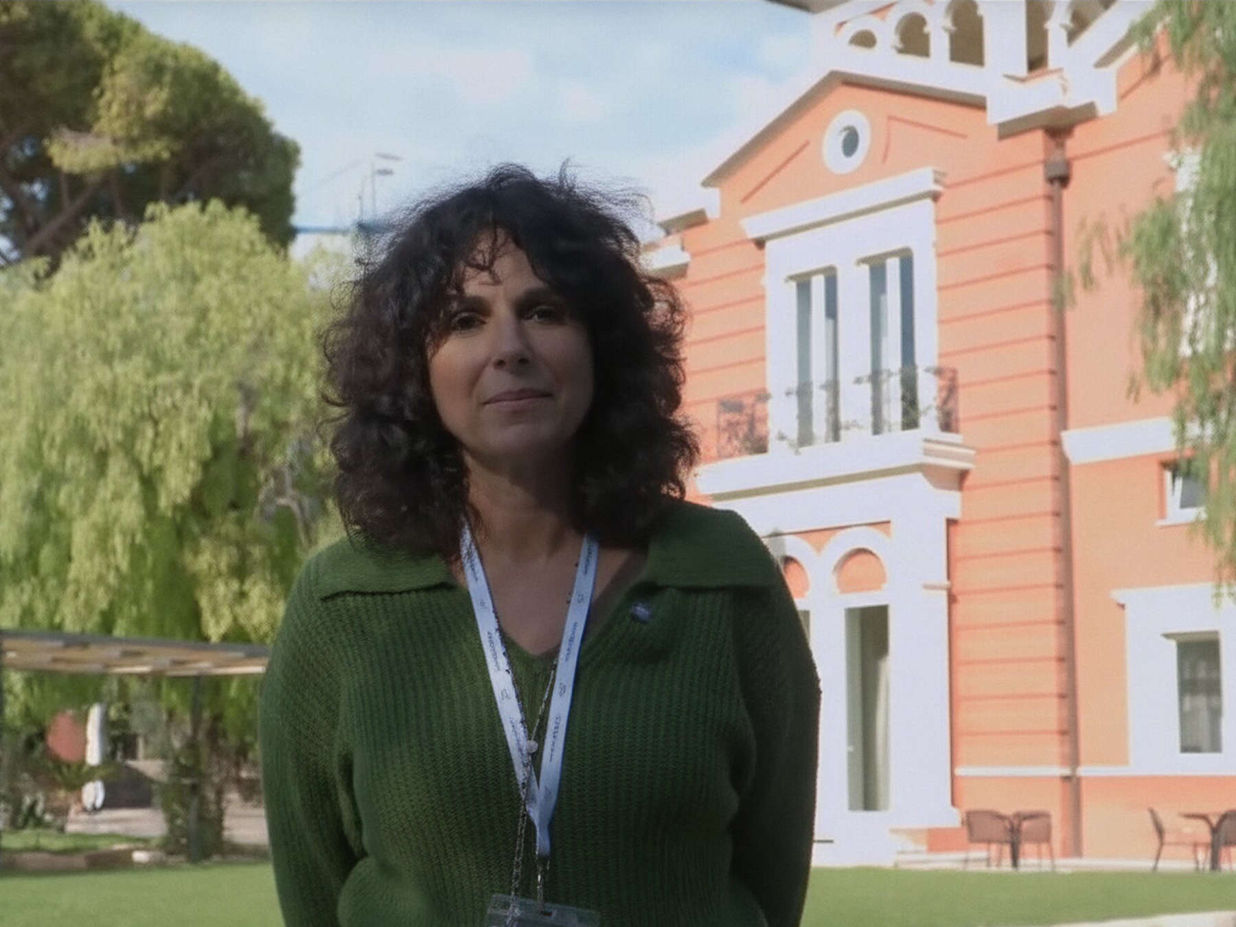 A woman in a green sweater stands in front of a building.